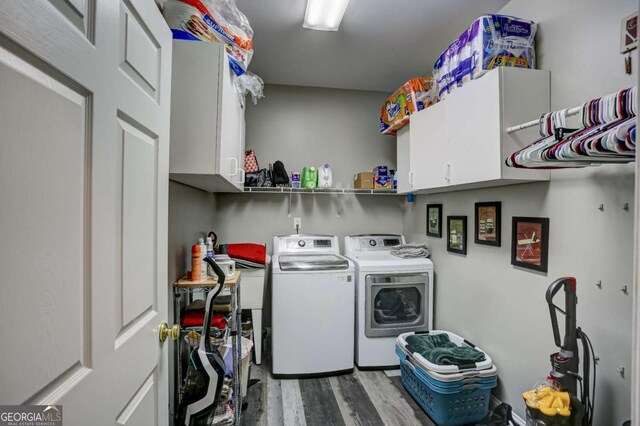 washroom with washing machine and clothes dryer, cabinet space, and wood finished floors