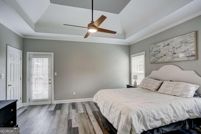 bedroom featuring baseboards, a tray ceiling, wood finished floors, and crown molding