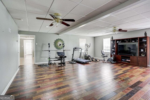 exercise room featuring a paneled ceiling, wood finished floors, baseboards, and a ceiling fan