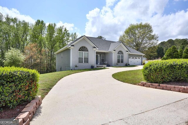 ranch-style house featuring a front yard, an attached garage, brick siding, and curved driveway