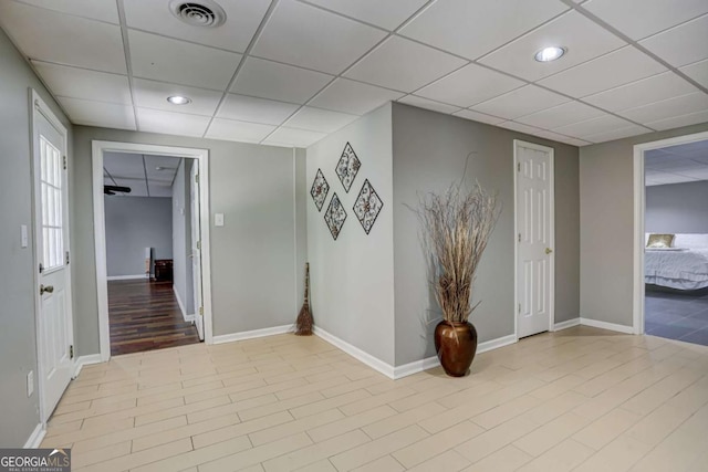 hallway featuring baseboards, visible vents, recessed lighting, and a drop ceiling