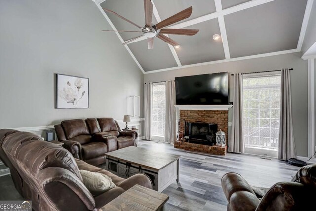 living area with a wealth of natural light, high vaulted ceiling, a ceiling fan, and a brick fireplace