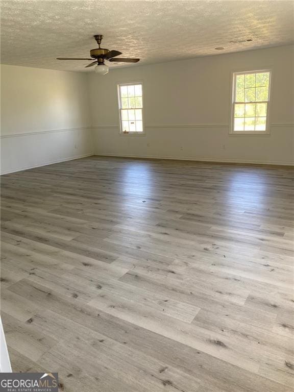 unfurnished room with baseboards, wood finished floors, ceiling fan, and a textured ceiling