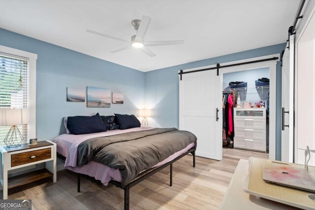 bedroom with a closet, a barn door, a spacious closet, light wood-style floors, and ceiling fan
