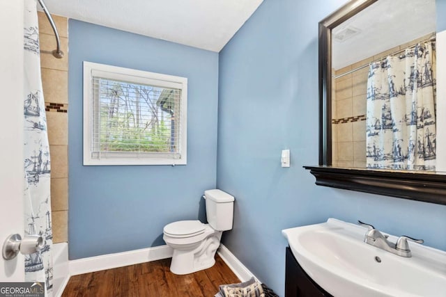 bathroom featuring toilet, vanity, wood finished floors, shower / bath combo with shower curtain, and baseboards