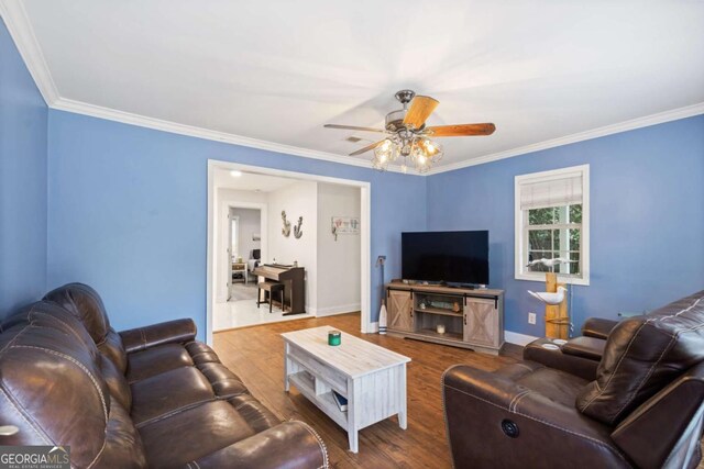 living room featuring a ceiling fan, crown molding, baseboards, and wood finished floors