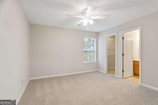 unfurnished bedroom with a closet, a textured ceiling, baseboards, a walk in closet, and light colored carpet
