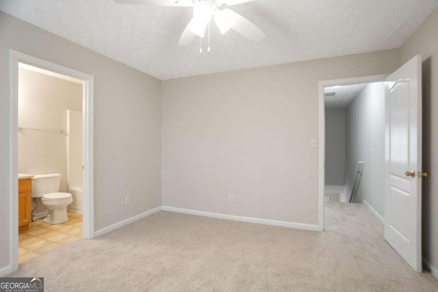 unfurnished bedroom featuring ensuite bathroom, a textured ceiling, baseboards, ceiling fan, and light carpet