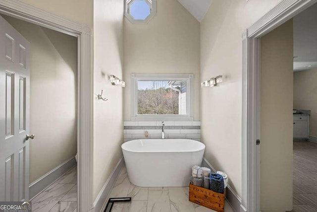 1768 Hood Rd, Dacula, GA 30019 - bathroom featuring marble look tiles, a freestanding bath, baseboards, and vaulted ceiling