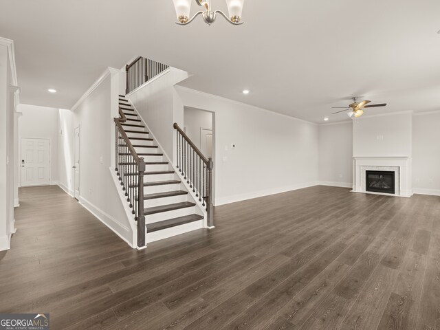 unfurnished living room with ceiling fan with notable chandelier, stairs, and crown molding