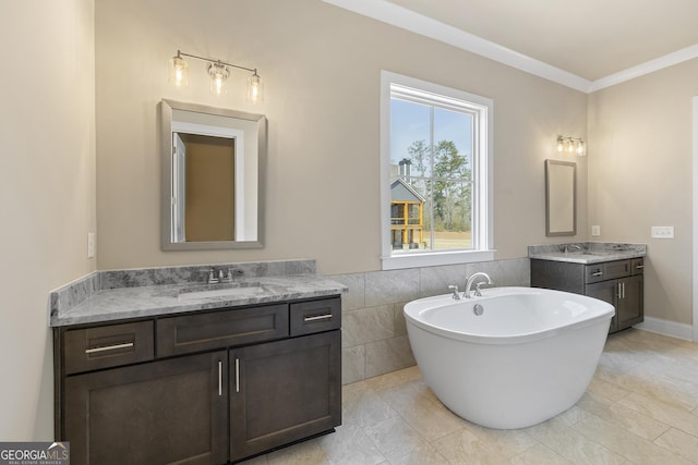full bath with a freestanding tub, crown molding, a sink, two vanities, and tile walls