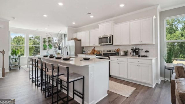 kitchen with a kitchen bar, appliances with stainless steel finishes, a kitchen island with sink, white cabinets, and dark wood-style flooring