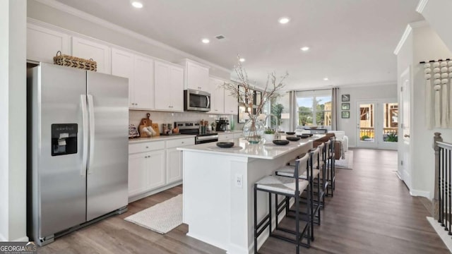 kitchen featuring crown molding, stainless steel appliances, backsplash, an island with sink, and white cabinets