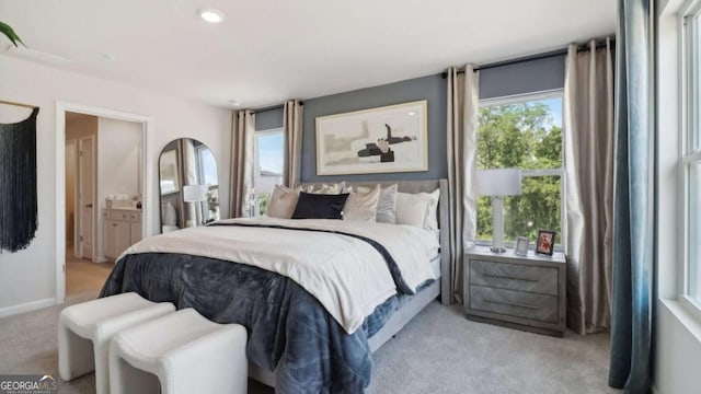 bedroom featuring connected bathroom, multiple windows, light colored carpet, and baseboards