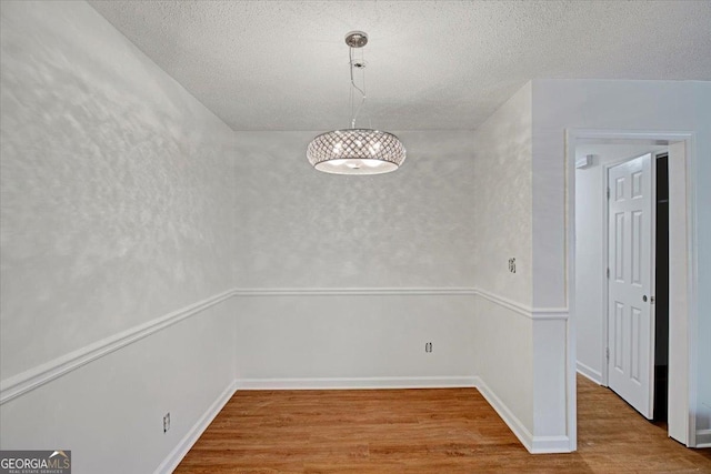 unfurnished dining area featuring a textured ceiling and wood finished floors