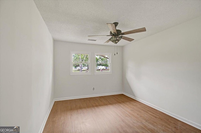 empty room with baseboards, a textured ceiling, visible vents, ceiling fan, and wood finished floors