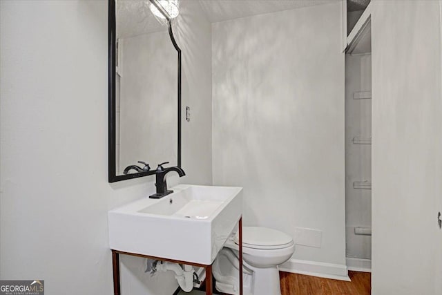 half bathroom with toilet, wood finished floors, a sink, and baseboards