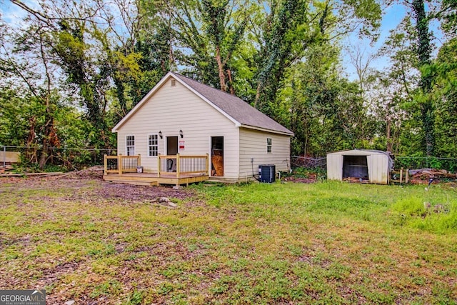 back of house with a yard, central AC unit, a wooden deck, and an outbuilding