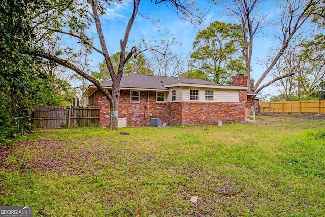 back of property featuring brick siding, fence, a yard, and a chimney