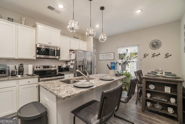 kitchen with decorative backsplash, visible vents, a sink, stainless steel appliances, and an island with sink