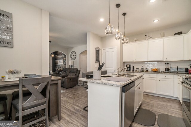 kitchen featuring decorative backsplash, a kitchen bar, arched walkways, a sink, and stainless steel appliances