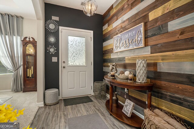 entrance foyer featuring wooden walls, baseboards, a notable chandelier, and wood finished floors