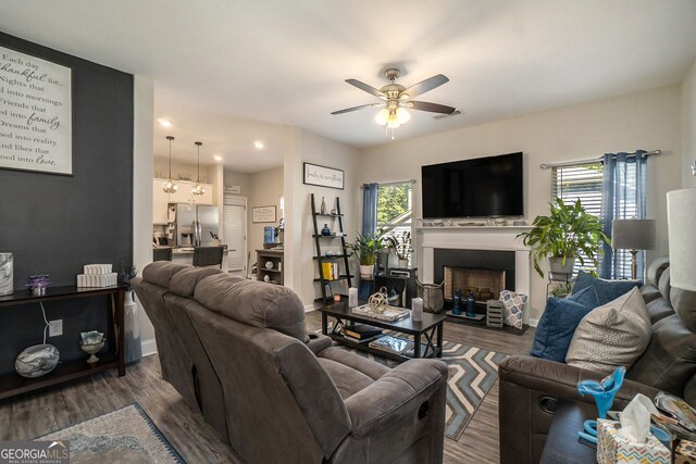living room featuring ceiling fan, visible vents, a fireplace, baseboards, and dark wood-type flooring