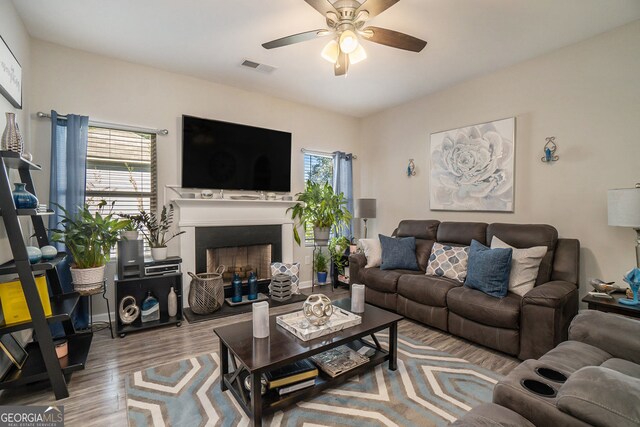 living area with visible vents, a ceiling fan, a fireplace with raised hearth, and wood finished floors