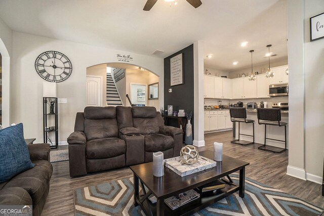 living room with dark wood-style flooring, arched walkways, a ceiling fan, baseboards, and stairway
