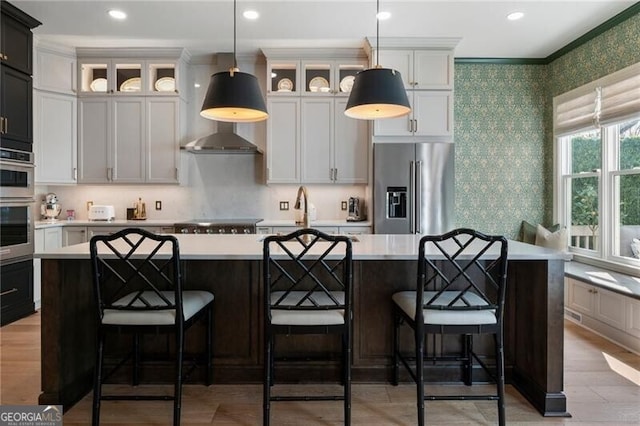 2630 Milford Ln, Alpharetta, GA 30009 - kitchen featuring appliances with stainless steel finishes, light countertops, wallpapered walls, a center island with sink, and glass insert cabinets