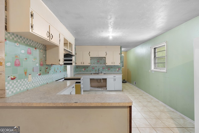 kitchen with tasteful backsplash, a sink, light countertops, a peninsula, and a textured ceiling