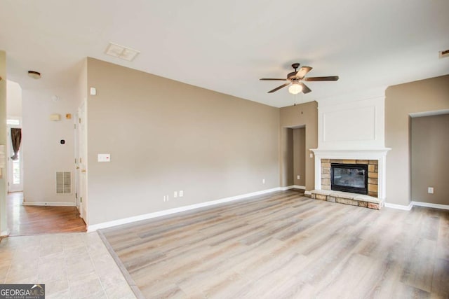 unfurnished living room with ceiling fan, a stone fireplace, light wood-style floors, and visible vents