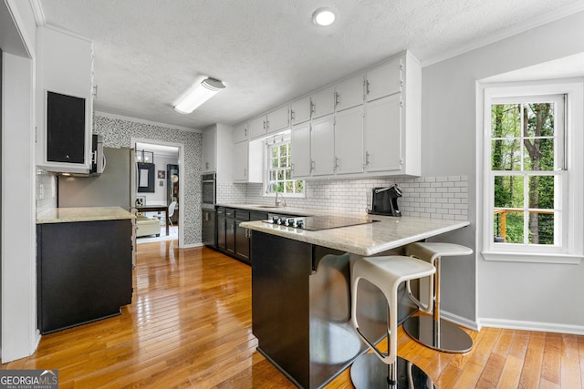 292 Old Rosser Rd, Stone Mountain, GA 30087 - kitchen with decorative backsplash, a peninsula, black electric stovetop, light wood-style floors, and stainless steel oven