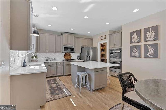 kitchen featuring light wood-type flooring, a breakfast bar, appliances with stainless steel finishes, a sink, and gray cabinetry