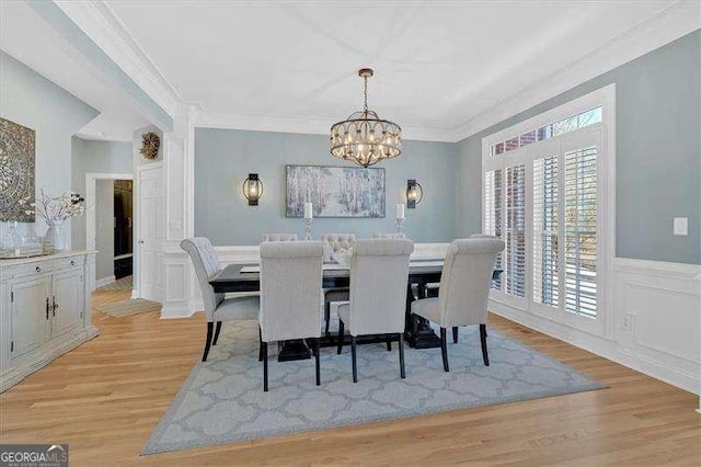 dining space with a chandelier, crown molding, light wood-style floors, wainscoting, and a decorative wall