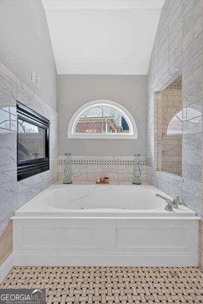 full bathroom with tile walls, a bath, a premium fireplace, and lofted ceiling