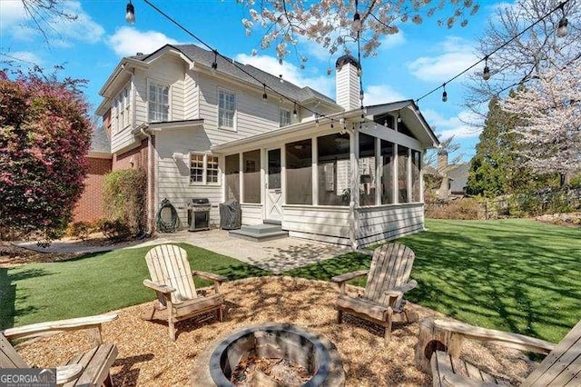back of house with a chimney, a patio area, an outdoor fire pit, a sunroom, and a lawn