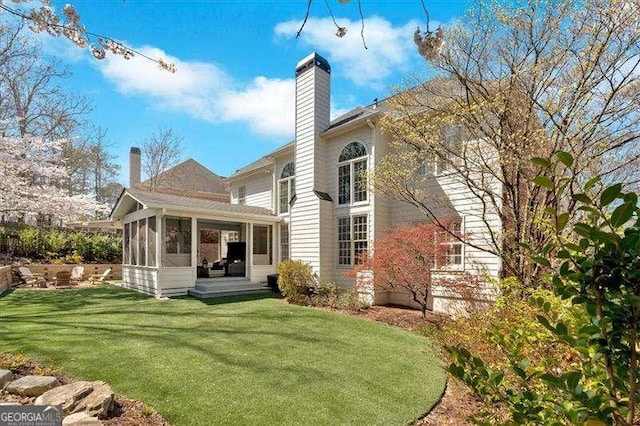 rear view of property featuring a sunroom, a lawn, and a chimney