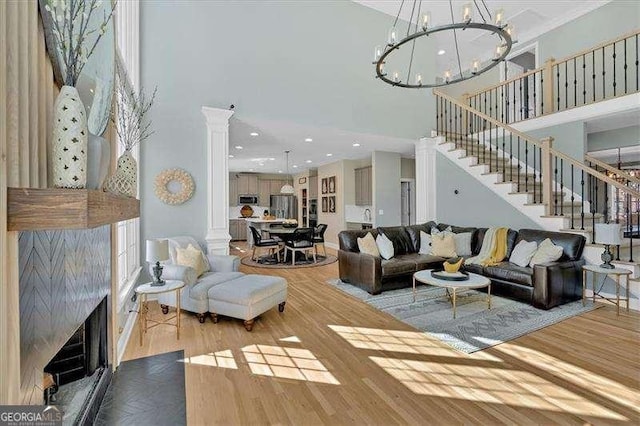 living room featuring an inviting chandelier, a high ceiling, stairs, decorative columns, and wood finished floors