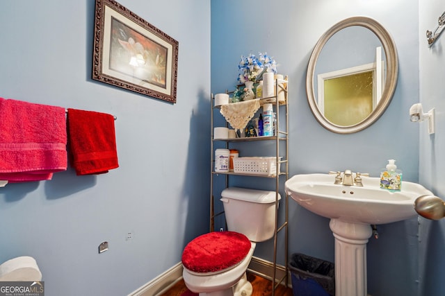 half bathroom with a sink, toilet, wood finished floors, and baseboards