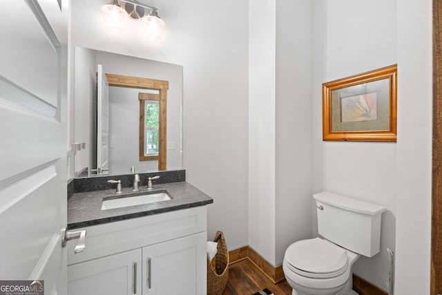 bathroom with toilet, wood finished floors, baseboards, and vanity