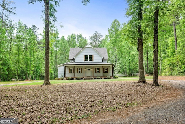 view of front of home with covered porch, fence, and a view of trees