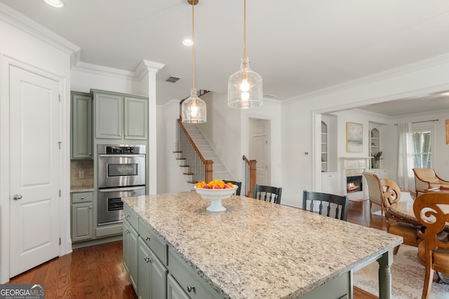 kitchen with gray cabinets, a kitchen island, dark wood-style flooring, light stone countertops, and double oven