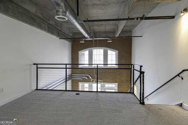 carpeted spare room featuring baseboards, a high ceiling, brick wall, visible vents, and track lighting