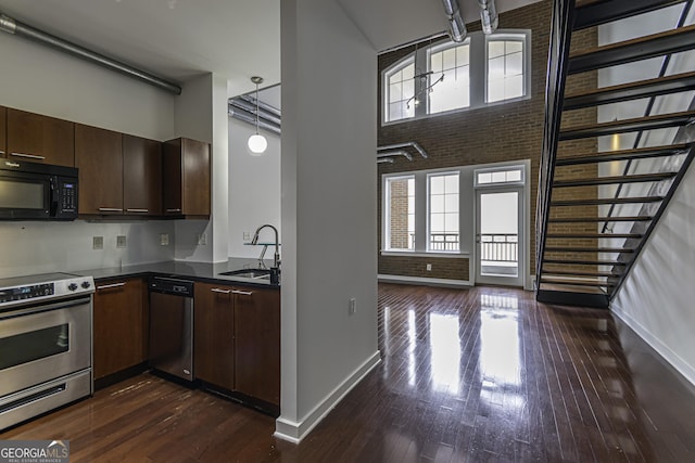 kitchen featuring a sink, a high ceiling, dark wood-style floors, stainless steel appliances, and dark countertops
