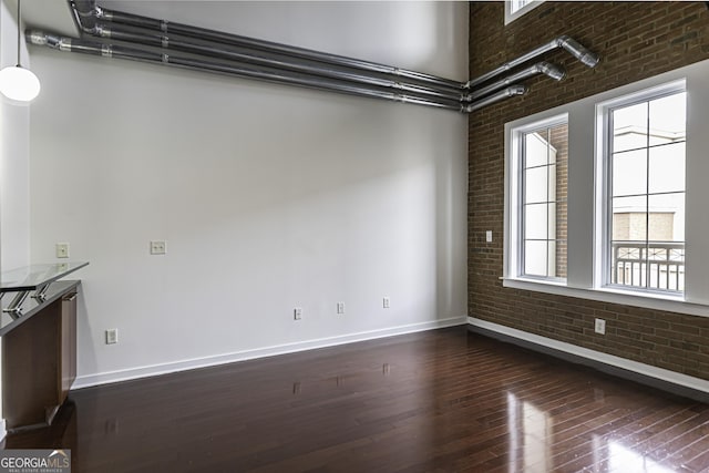 empty room featuring dark wood-style flooring, a towering ceiling, baseboards, and brick wall