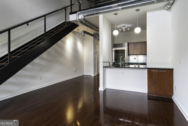 kitchen with decorative light fixtures, built in refrigerator, dark wood-type flooring, baseboards, and dark countertops