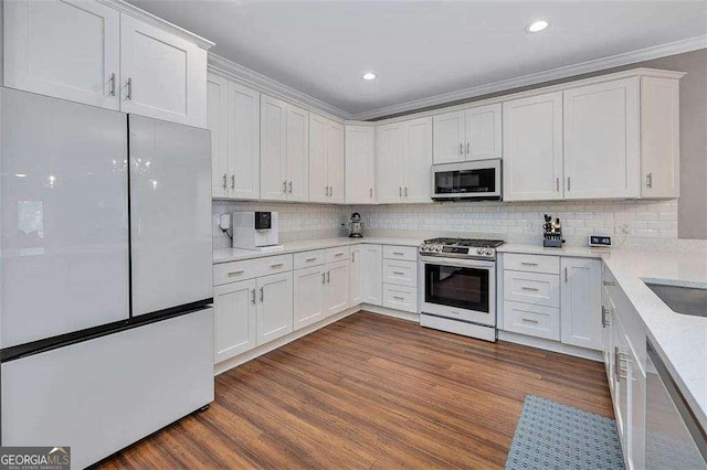 123 E Commons Dr, Saint Simons, GA 31522 - kitchen with appliances with stainless steel finishes, dark wood-style floors, tasteful backsplash, white cabinetry, and crown molding