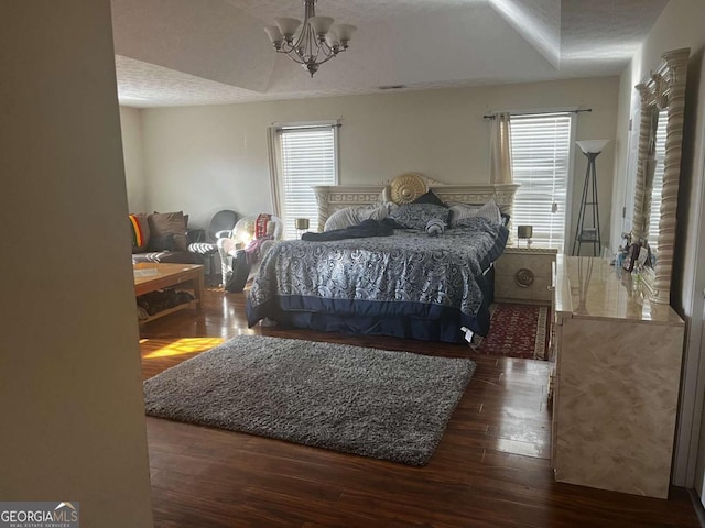 bedroom featuring multiple windows, a notable chandelier, wood finished floors, and a textured ceiling