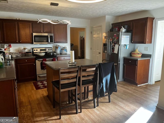 kitchen with a textured ceiling, a kitchen island, dark countertops, light wood-style flooring, and appliances with stainless steel finishes